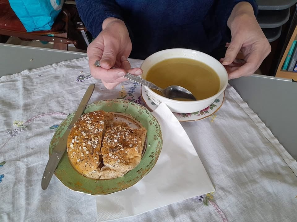 Someone eating soup with a roll